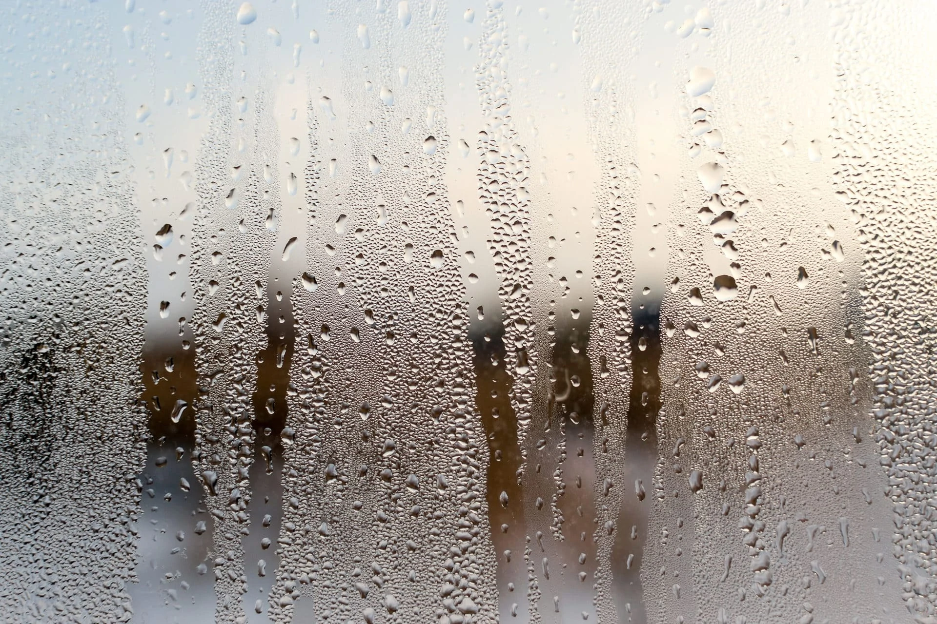 Condensation forms water droplets on the surface of a clear glass house interior window. Defocused background texture provides a brown colour. Copy space area for architecture domestic concepts and backdrops.